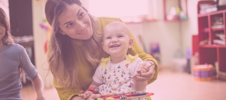 a person smiles while holding a baby in a playroom