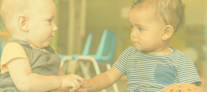 Two babies sitting on the floor holding hands