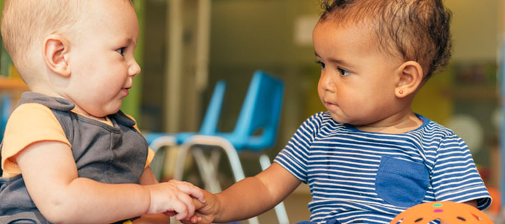 Two babies holding hands in a classroom.