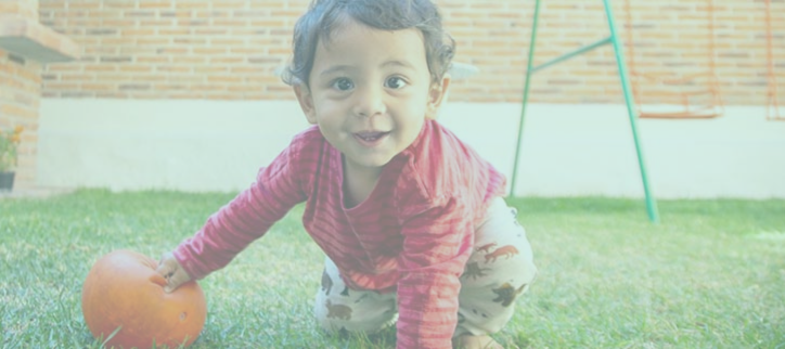 a baby crawling on the grass with an orange pumpkin