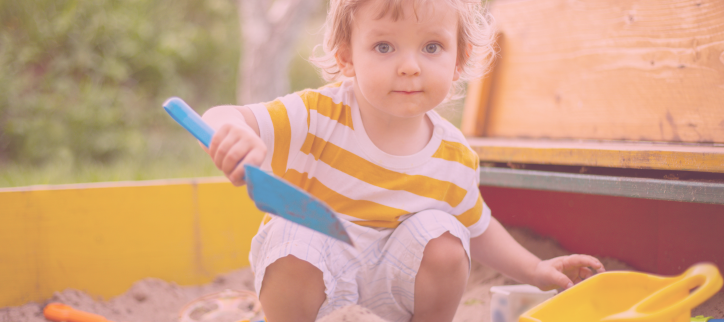 a toddler playing in a sandbox with a toy shovel