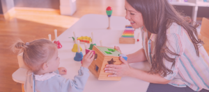 caregiver laughing while handing a toddler a toy